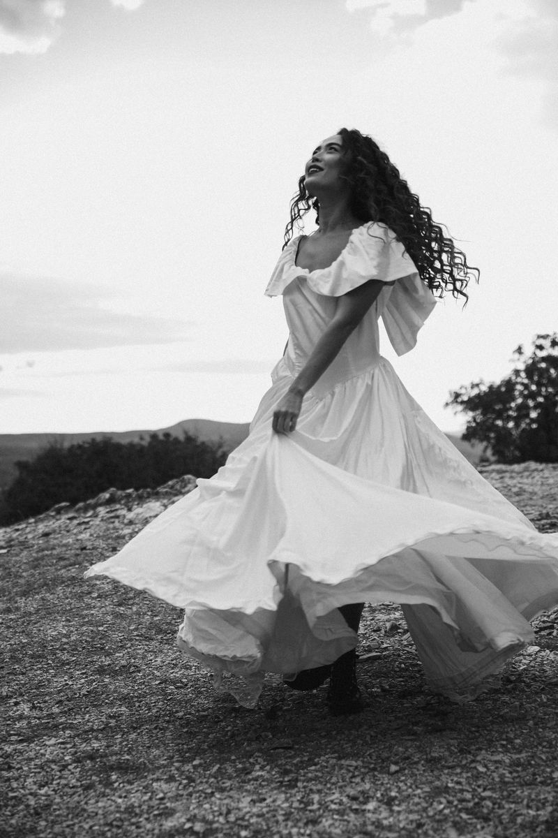 Black and white: a woman in a white dress spinning on a hilltop, the skirt flying out