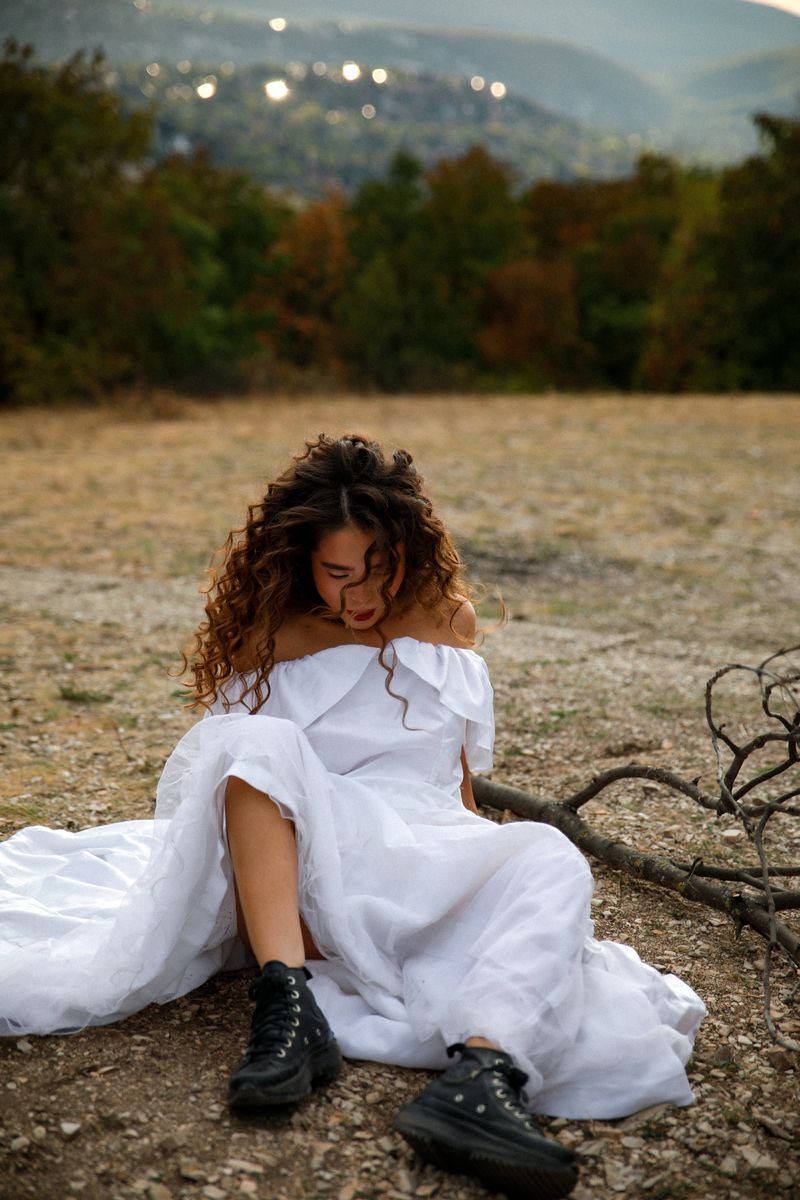 A woman in a white dress and black boots sitting on dry grass