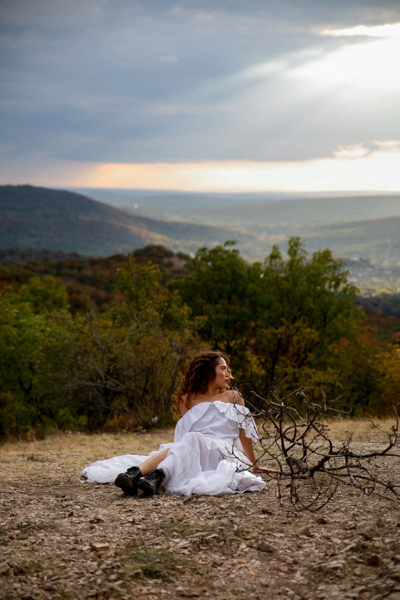 A woman in a white dress sitting on a hillside above a valley