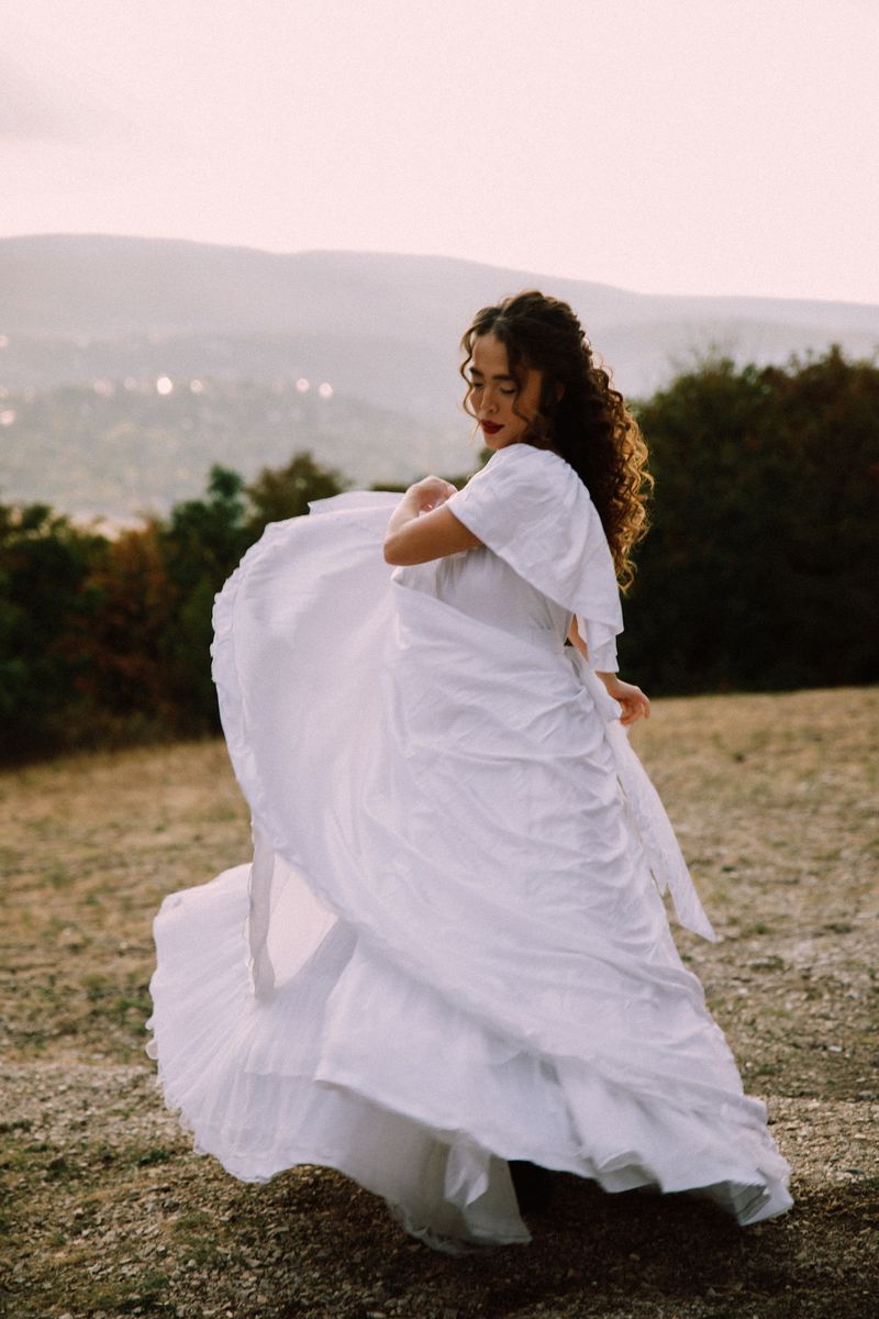 A woman in a white dress twirling on a hill above the city