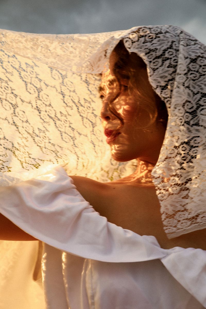 A woman under a lace veil, sunlight falling through the lace onto her face
