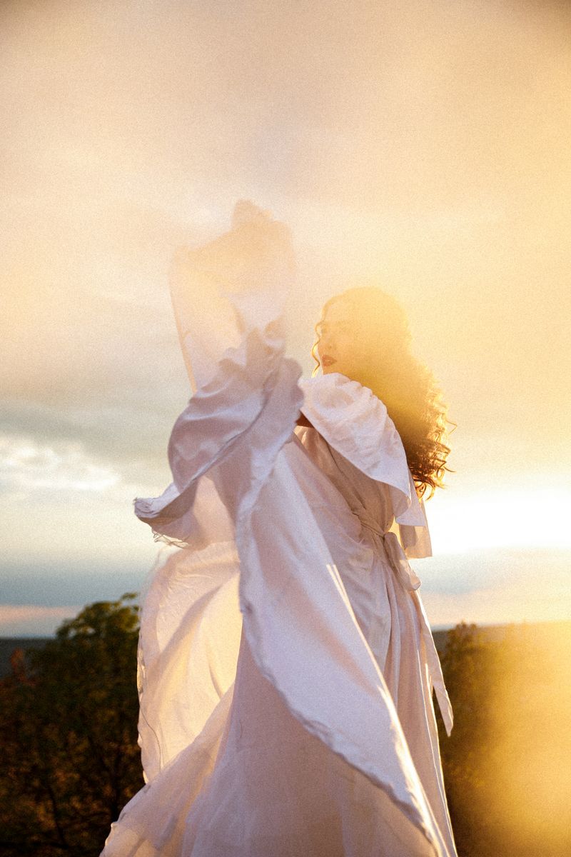 A woman in a white dress lifting the fabric into the low sun