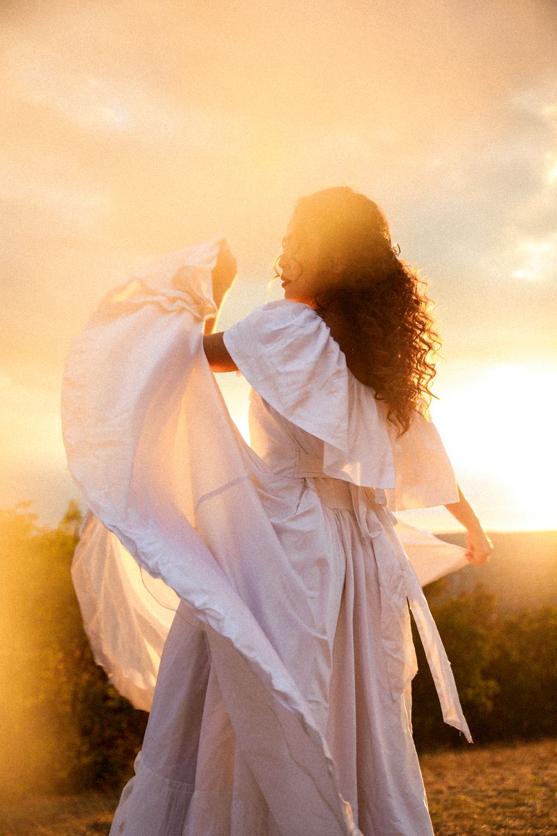 A woman in a white dress lifting the fabric against the setting sun