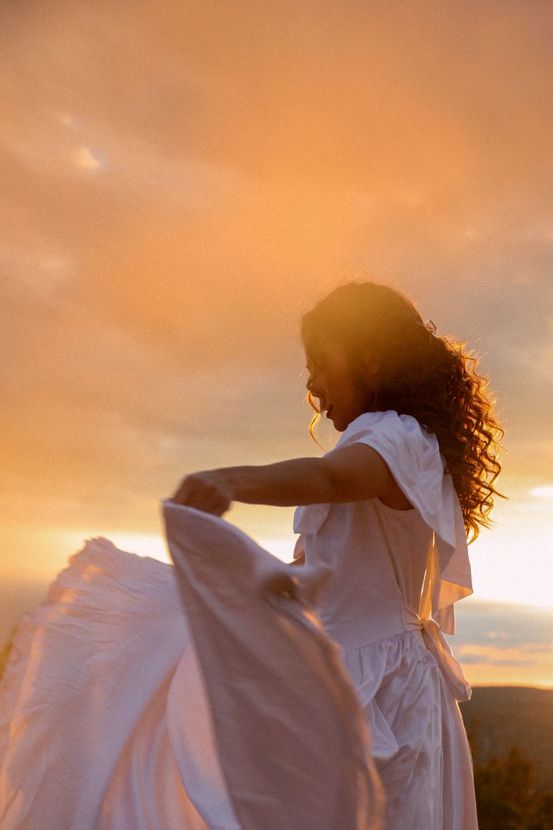 A woman gathering her white skirt in golden evening light