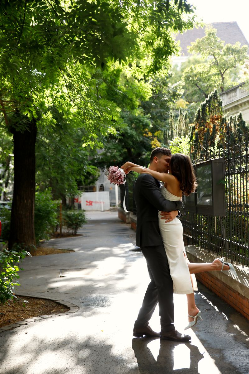 A couple dancing on a tree-lined street, she raises the bouquet behind him