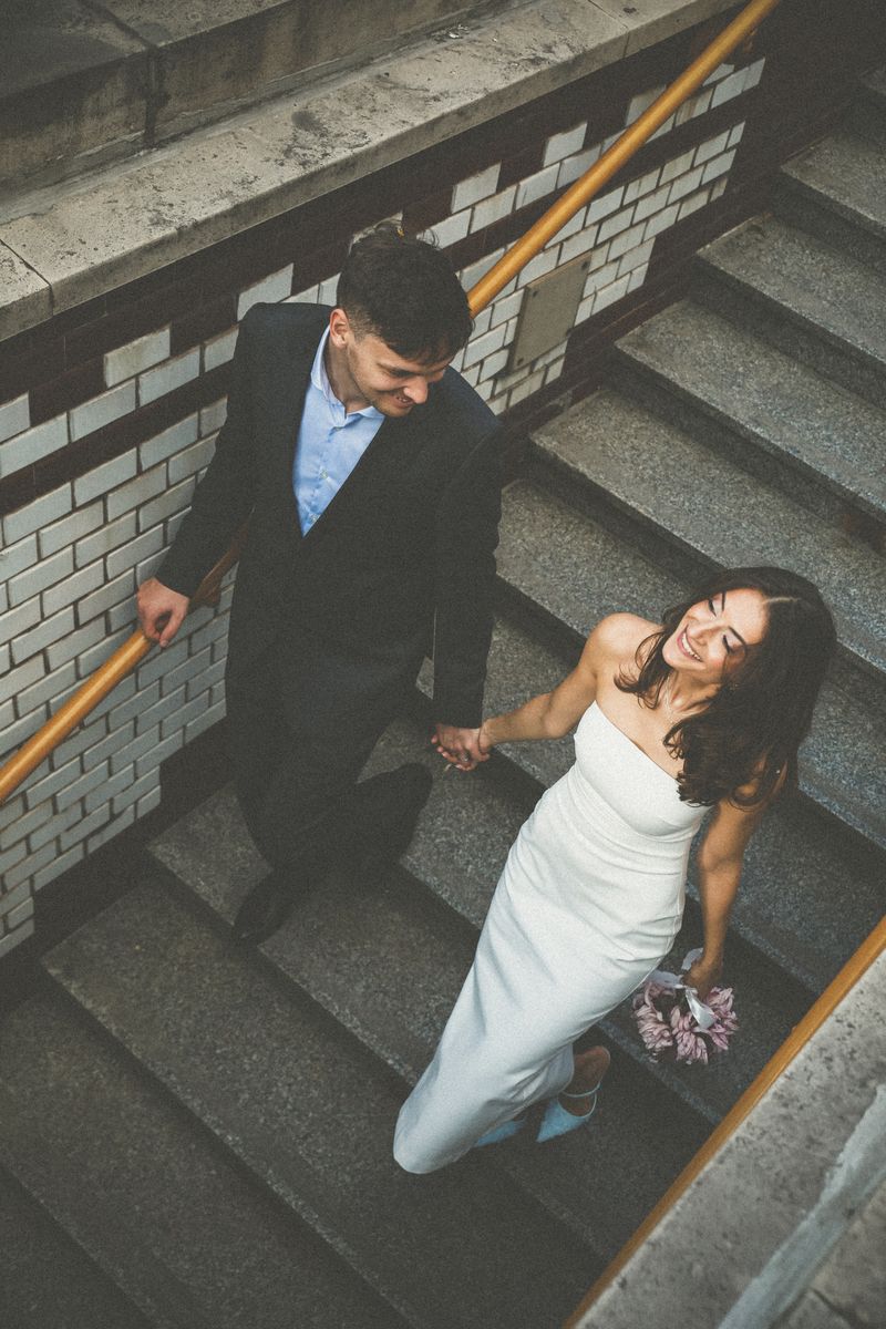 A couple on a tiled stairway, she looks up laughing with a bouquet in her hand