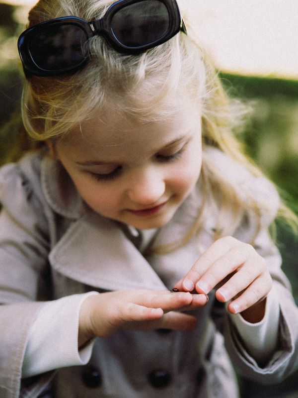 A little girl in sunglasses and a trench coat looking at her hands